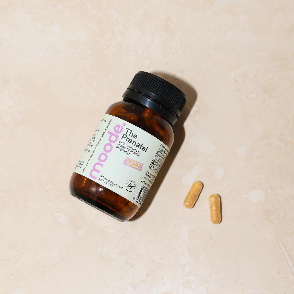 The Prenatal by moode, a 60 capsule amber glass bottle, lying beside two capsules on a cream stone surface.