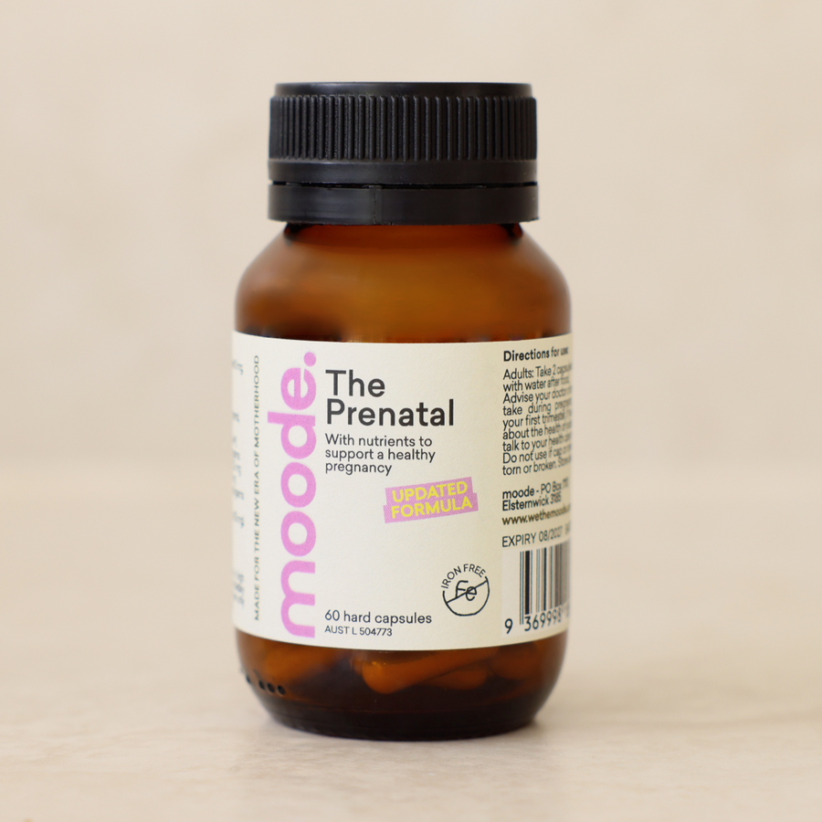The Prenatal by moode, a 60 capsule amber glass bottle, lying beside two capsules on a cream stone surface.