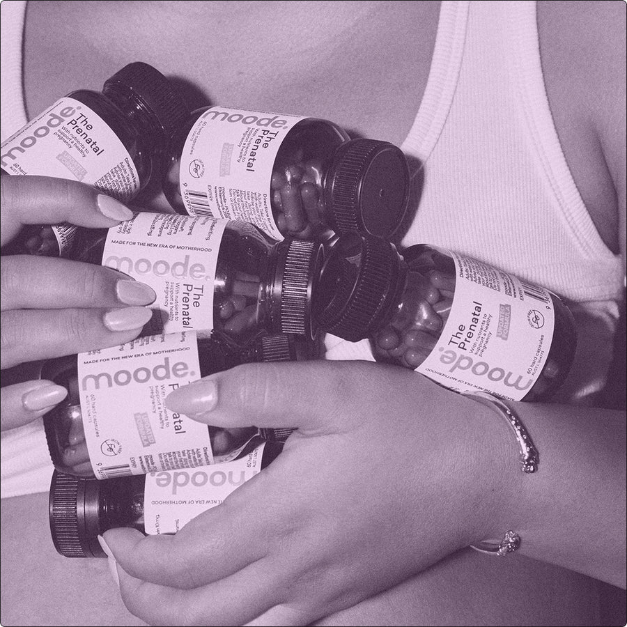 A close-up of a person holding several bottles of moode the prenatal a pregnacy multivitamin. 